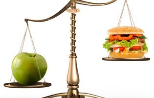 Apple and hamburger on scales conceptual Big green ripe apple and junk food hamburger on scales isolated white background